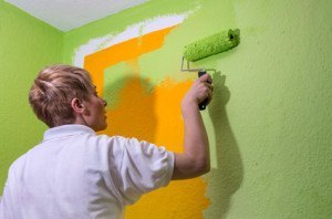 Malerin überstreicht die oragegefärbte Wand mit grüner Farbe